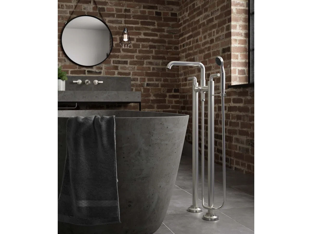 Modern bathroom with gray freestanding stone bathtub, black towel, brick wall, and stainless steel floor-mounted faucet.