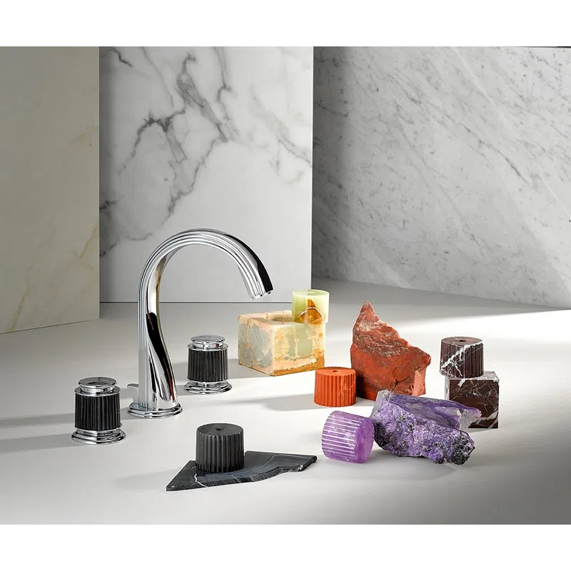 Chrome faucet surrounded by colorful mineral and stone samples on a marble surface with marble backdrops