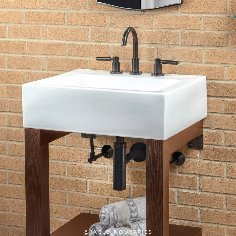 Modern white ceramic sink with black faucet and handles on wooden stand against brick wall.