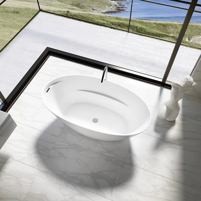 Modern white freestanding bathtub on marble floor with ocean view through glass walls and sculpture nearby