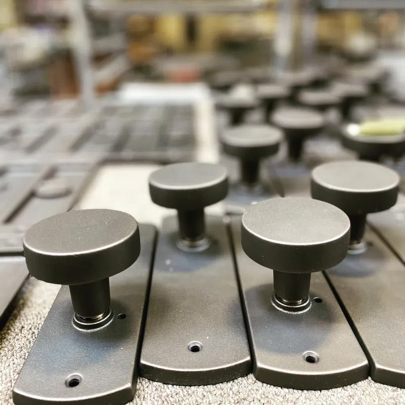 Close-up of multiple black round control knobs on matte rectangular plates arranged in rows on a textured surface.