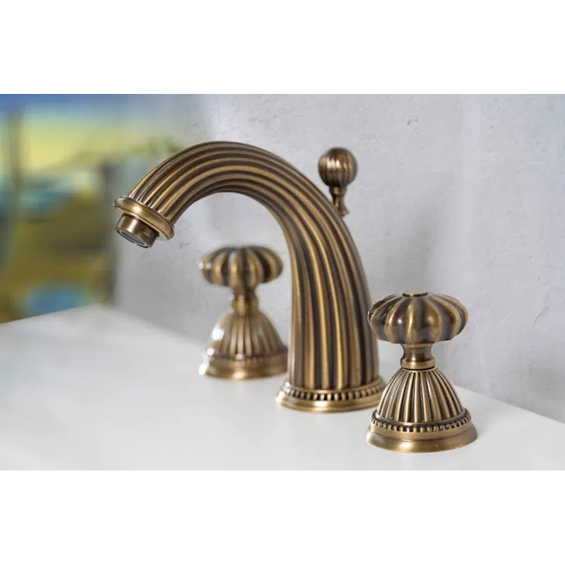Antique brass bathroom faucet with ornate design and dual handles mounted on a white sink against gray wall.