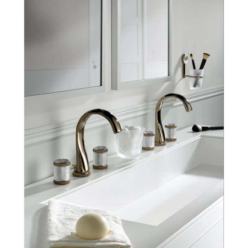 Modern double bathroom sink with sleek gold faucets, decorative jars, a white towel, and makeup brushes.