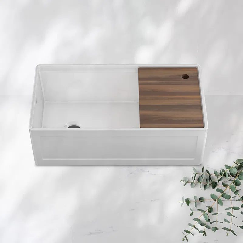 White kitchen sink with integrated wooden cutting board on a light marble surface with eucalyptus branch.