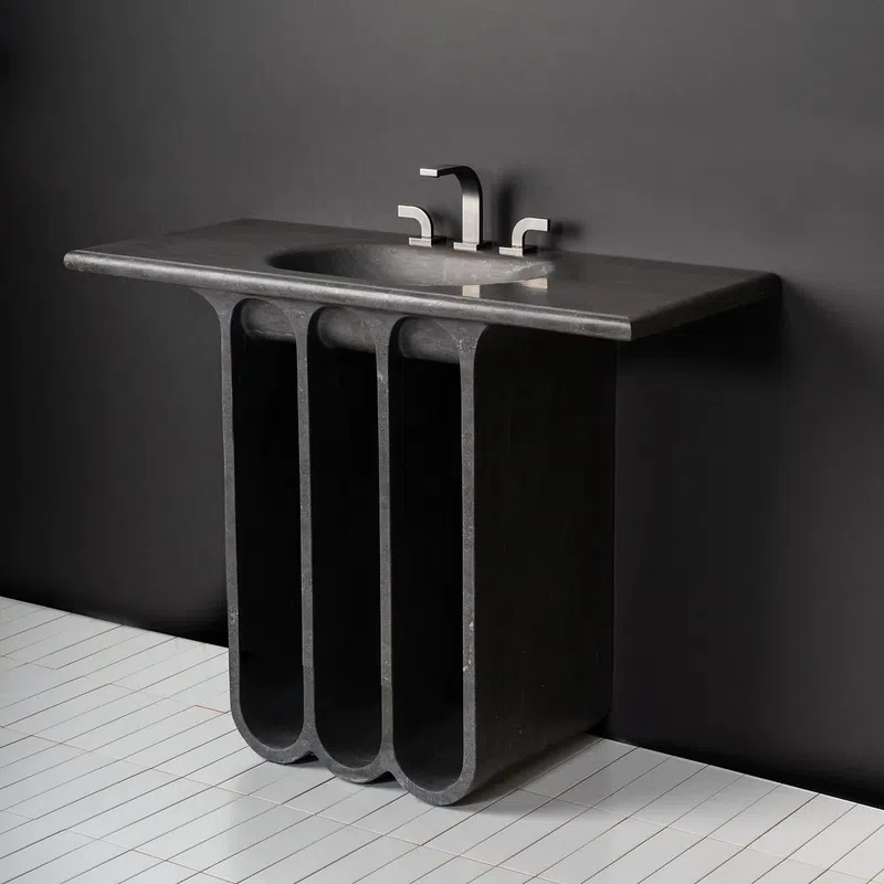 Modern black stone sink with sleek faucet mounted on a sculptural base against a dark wall.