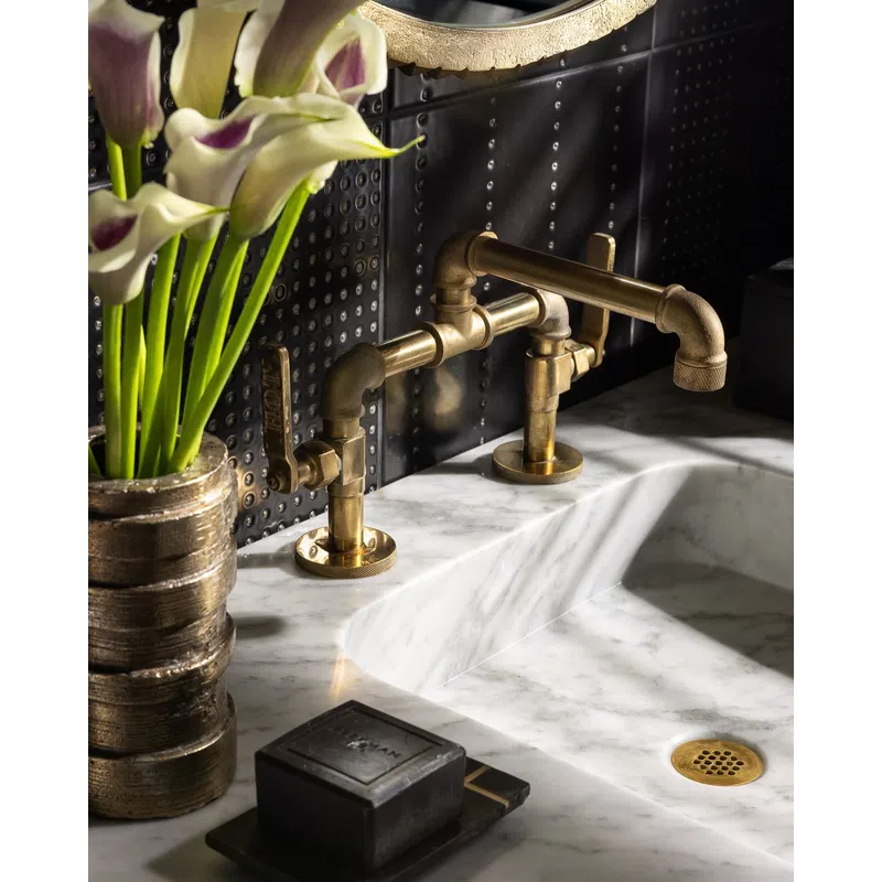 Brass industrial faucet on white marble sink with black soap and gold vase holding calla lilies