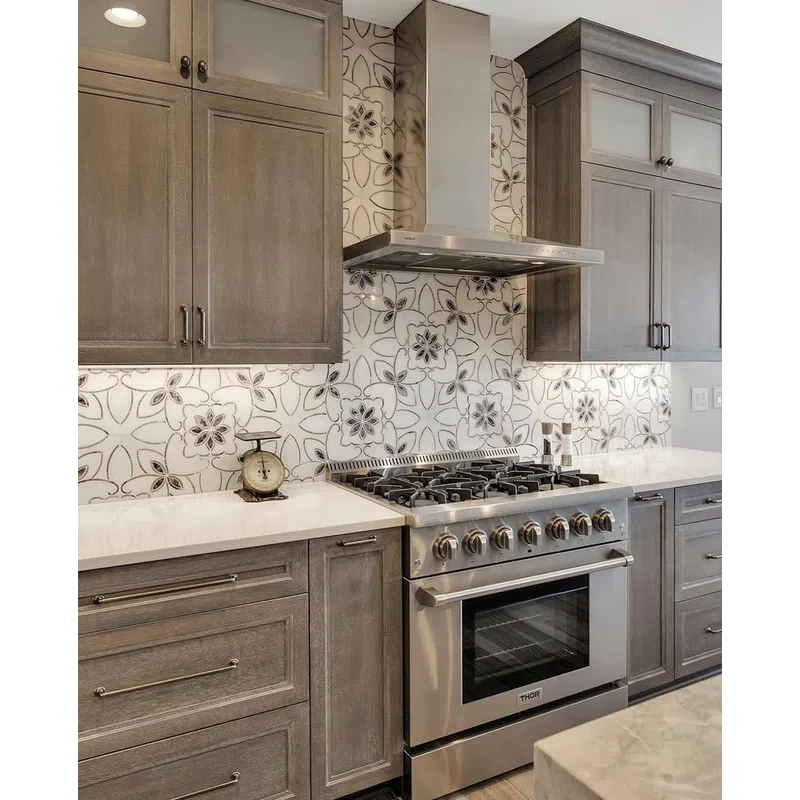 Modern kitchen with gray wood cabinets, stainless steel gas stove, and floral patterned tile backsplash.