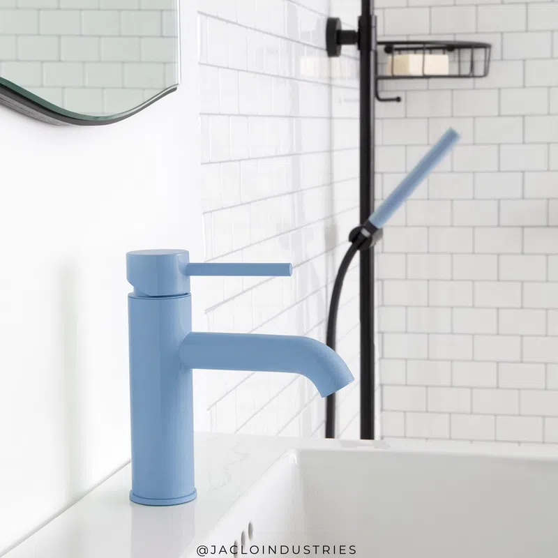 Matte blue bathroom faucet installed on white countertop with white subway tile wall and black shower fixture in background