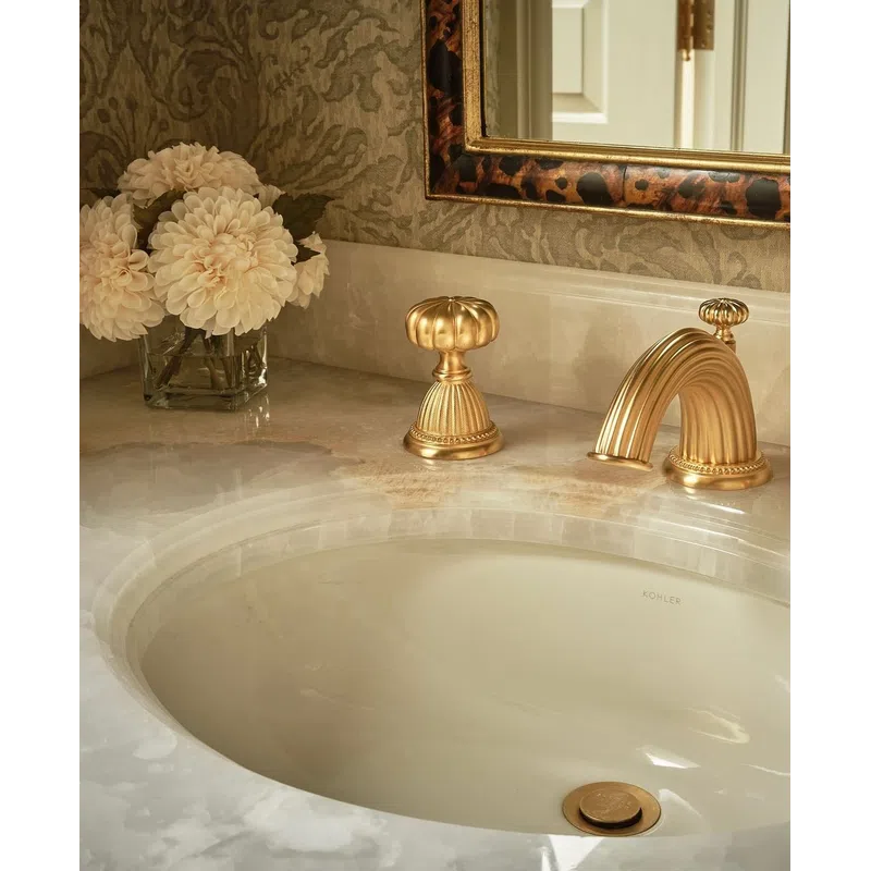 Elegant bathroom sink with gold faucet, ornate mirror, and a vase of white flowers on marble countertop.