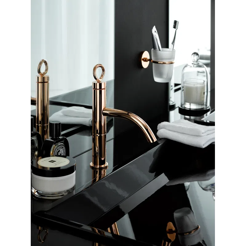 Modern bathroom sink with rose gold faucet, black countertop, toiletries, and white towels neatly arranged.