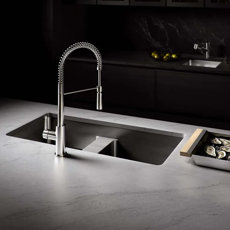 Modern kitchen sink with a sleek stainless steel spring coil faucet on a marble countertop with oysters on a tray.