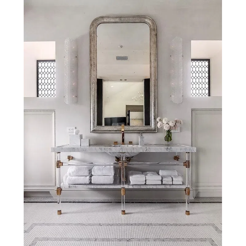 Elegant bathroom with a large arched mirror, marble countertop, clear vanity, and neatly stacked white towels.