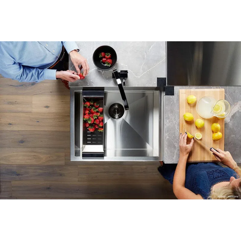 Top view of two people preparing strawberries and lemons on a kitchen counter with a modern stainless steel sink.