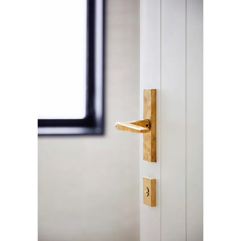 Close-up of modern gold door handle and lock on a white door near a window with soft natural light.