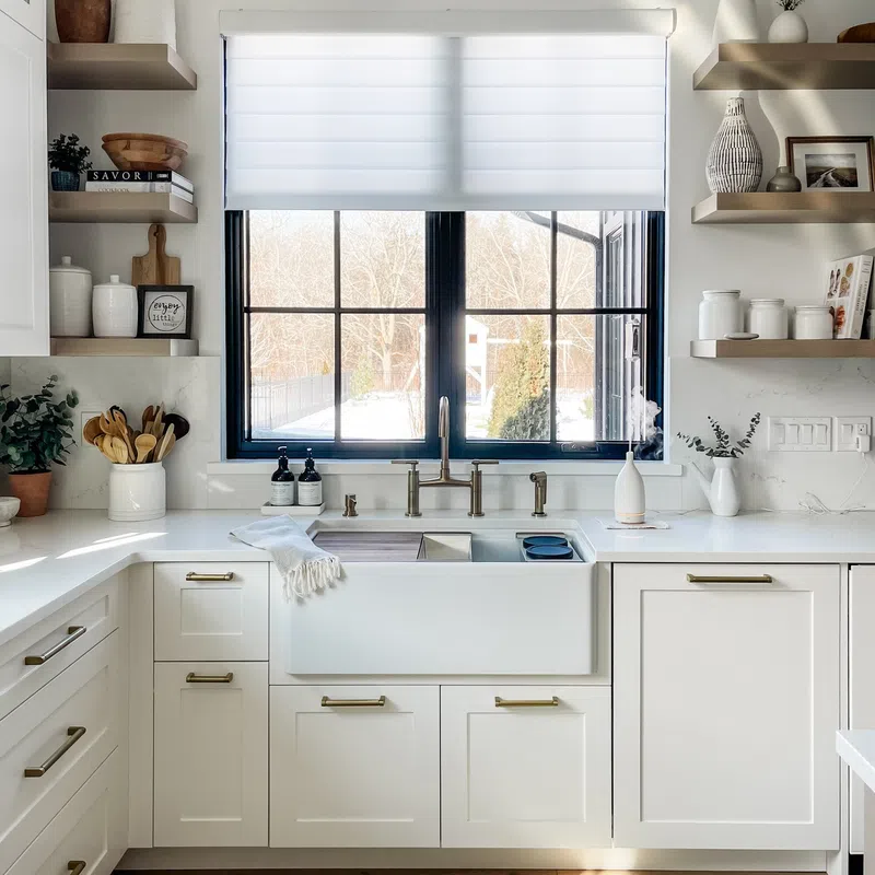 Bright modern kitchen with white cabinetry, farmhouse sink, brass fixtures, and large window overlooking snowy yard.