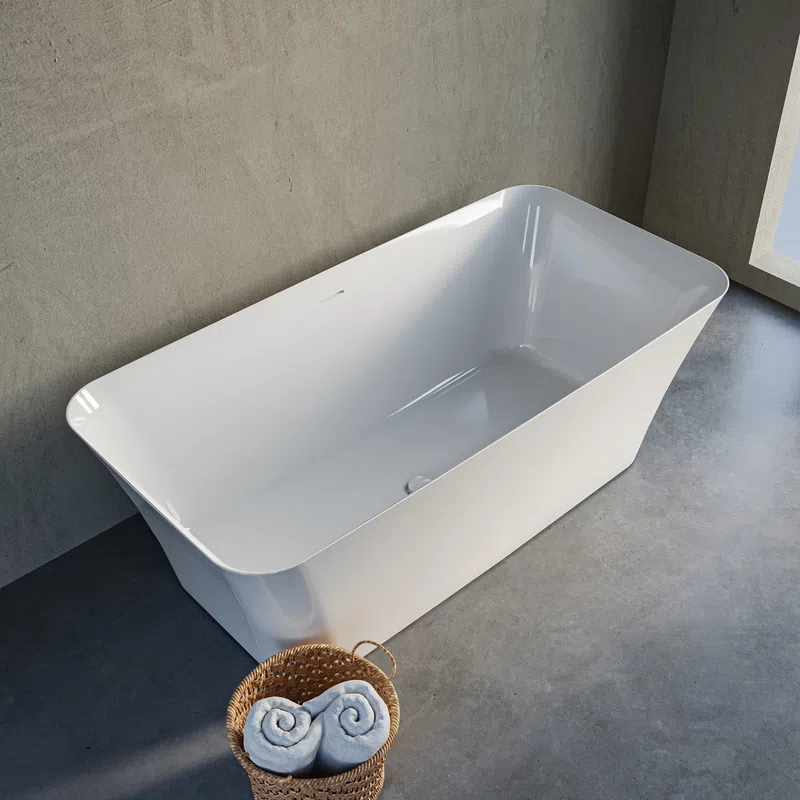 Modern white freestanding bathtub on concrete floor next to wicker basket with rolled towels in bright bathroom.