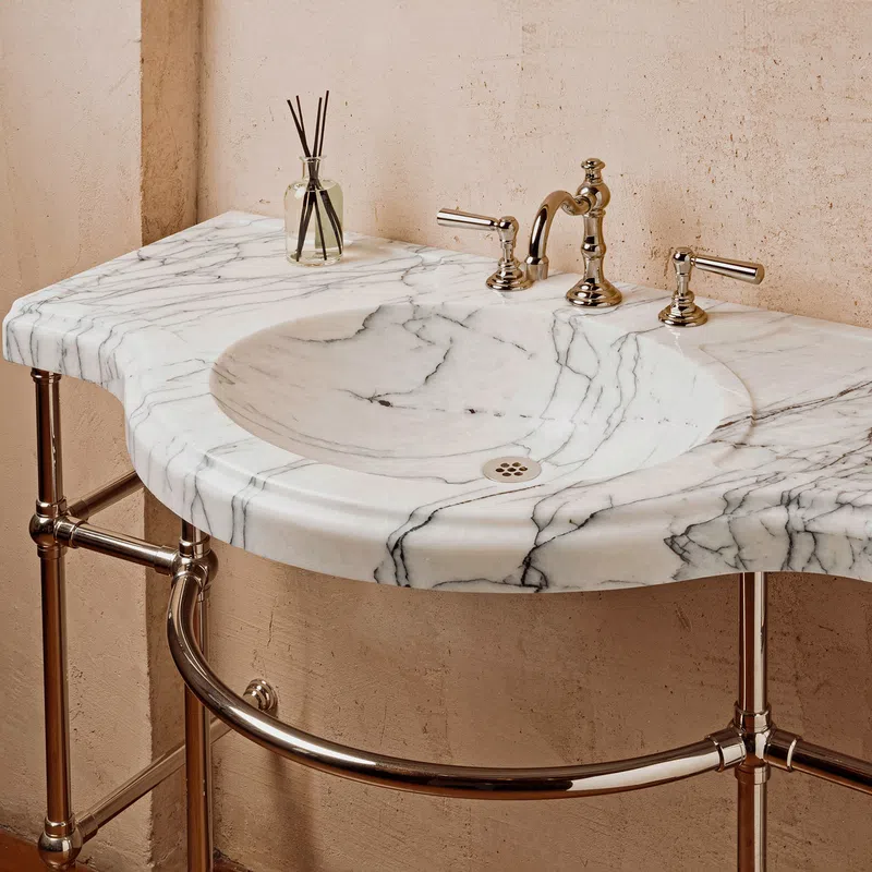 Marble bathroom sink with chrome faucet and vintage-style exposed pipe base against a beige wall