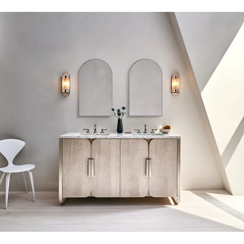 Modern bathroom vanity with dual sinks, arched mirrors, wall sconces, and minimalist white chair in natural light.