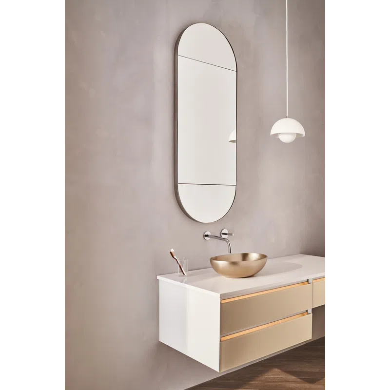 Minimalist bathroom with oval wall mirror, brass vessel sink, white floating vanity, and modern pendant light.
