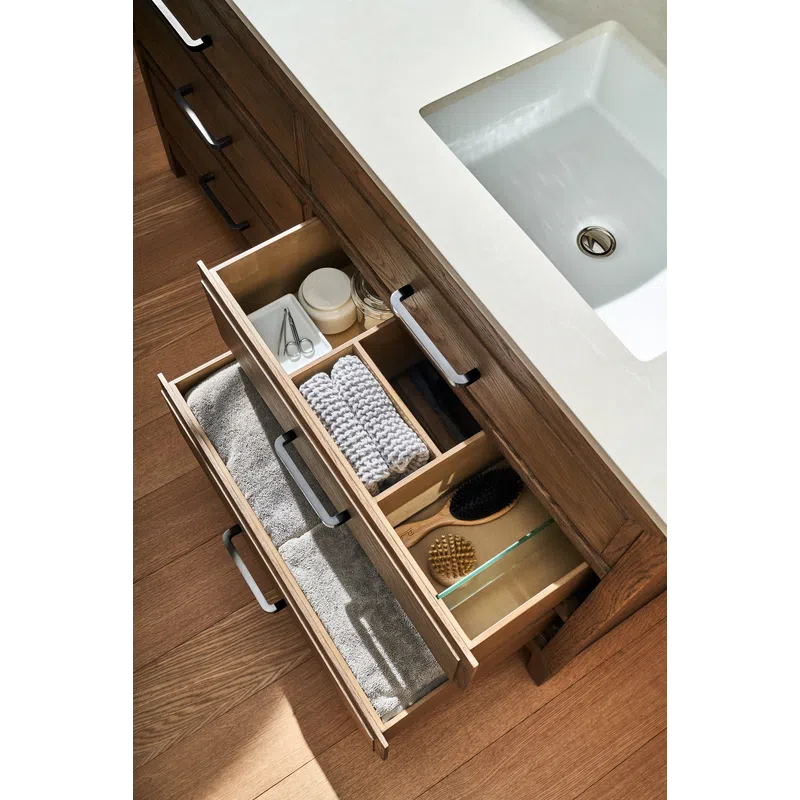 Open bathroom vanity drawers with towels, brushes, skincare jars, and grooming tools under a white sink.