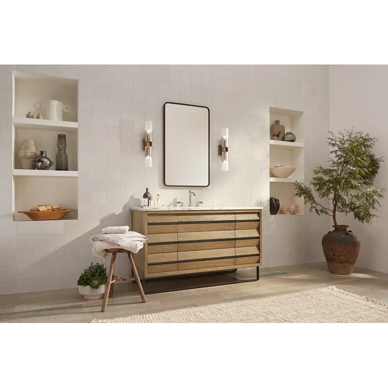 Modern bathroom with wooden vanity, rectangular wall mirror, decorative shelves, stool with towels, and large potted plant.