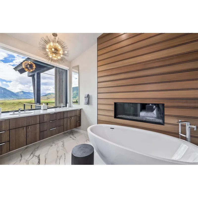 Modern bathroom with freestanding tub, wood panel fireplace, marble floor, large window, and double vanity.