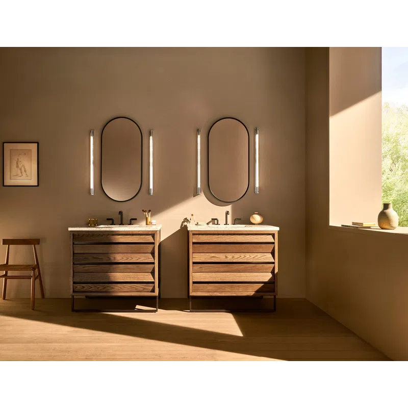 Modern bathroom with twin wooden vanities, oval mirrors, vertical lights, and natural sunlight through window.