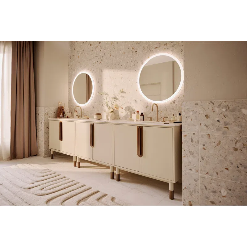 Modern bathroom with double vanity, round LED mirrors, brass faucets, and terrazzo wall tiles in soft beige tones