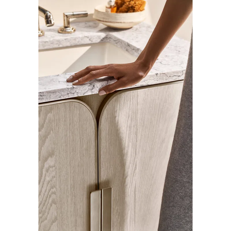 Close-up of a hand resting on a marble countertop above light wood cabinet doors with modern metal handles.