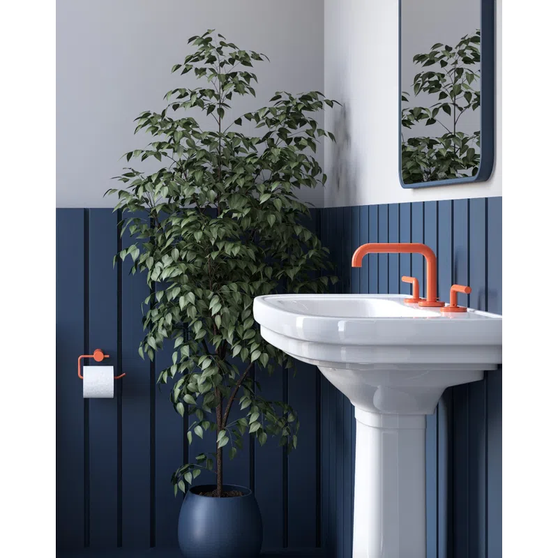 Modern bathroom corner with white pedestal sink, orange faucet, navy paneling, large potted plant, and wall mirror.