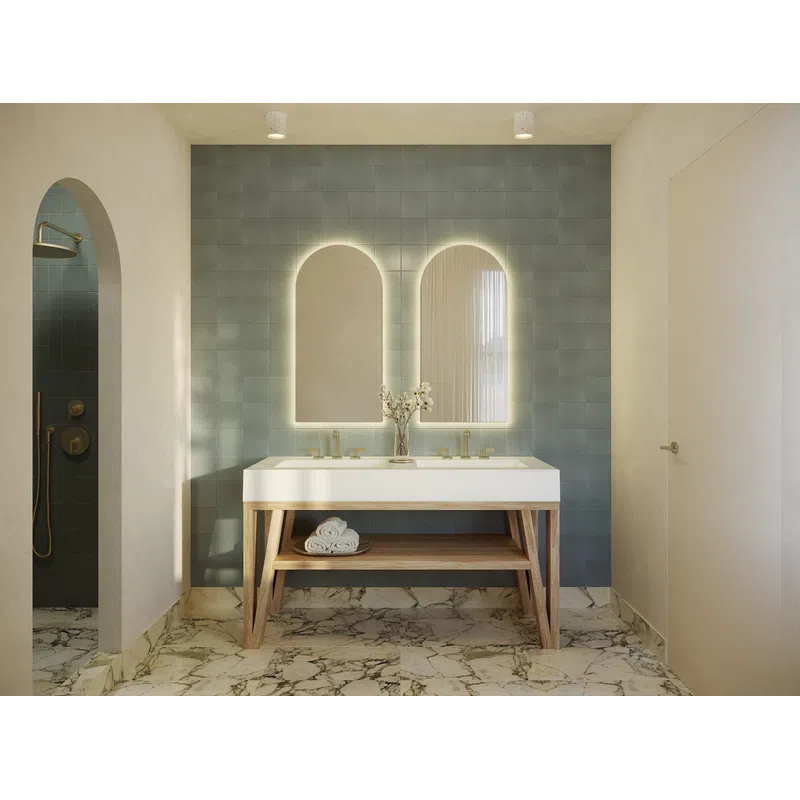 Modern bathroom with double sinks, backlit arched mirrors, blue tiled wall, wooden vanity, and marble floor.