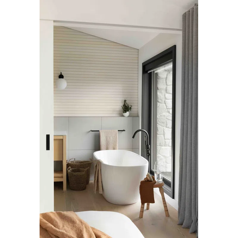 Modern minimalist bathroom with freestanding tub, wooden stool, large window, and neutral decor elements.