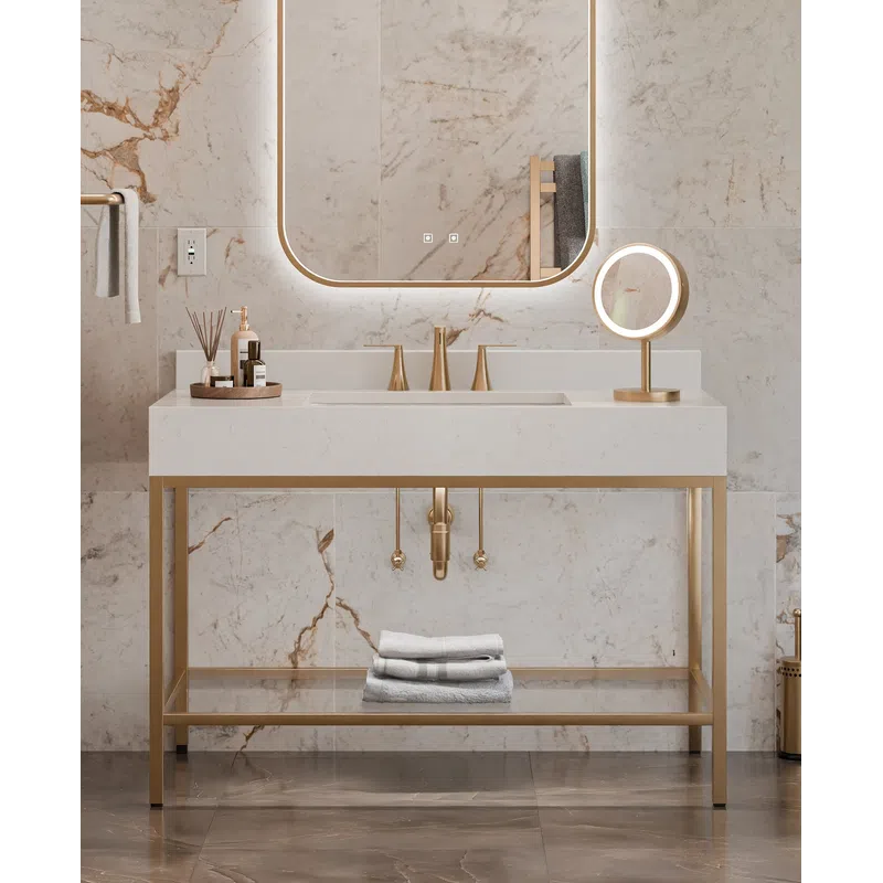 Modern bathroom sink with gold fixtures, illuminated mirror, marble walls, and neatly folded towels on shelf.