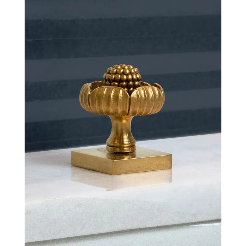 Ornate gold decorative knob with rounded petals and a textured spherical center on square base.