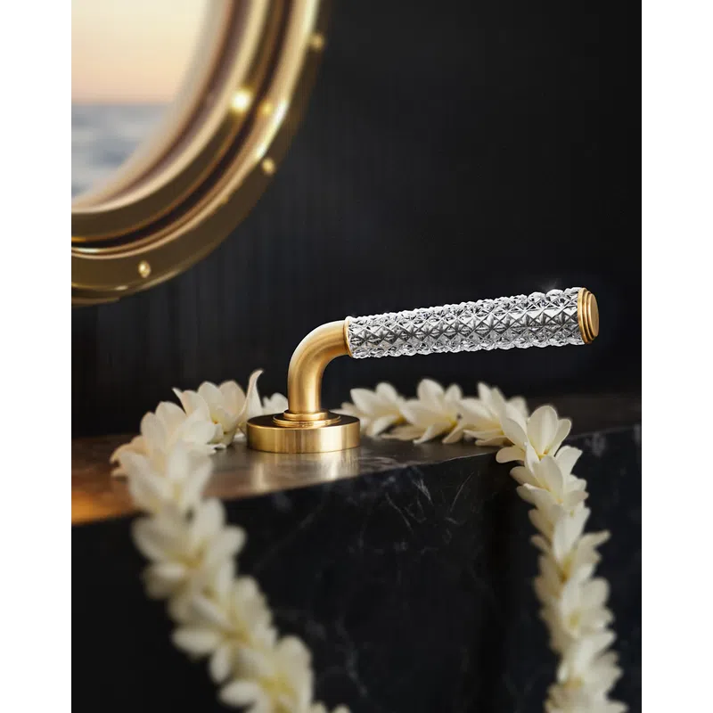 Elegant gold and crystal door handle on black marble surface decorated with white flower garland under a round mirror.