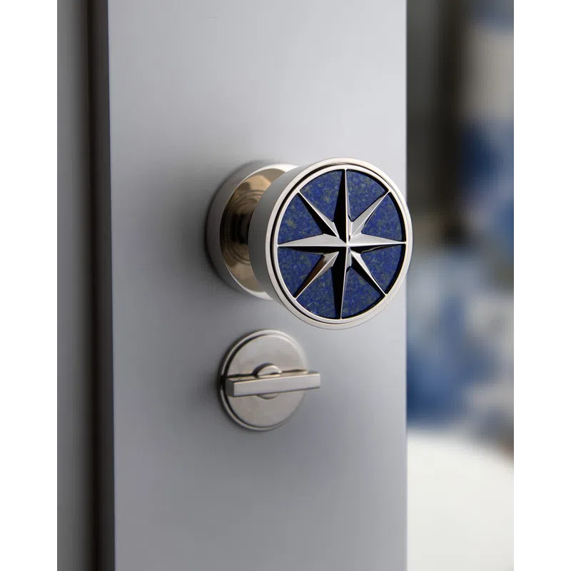 Close-up of a stylish door knob featuring a blue compass star design with a silver lock below on a gray door.