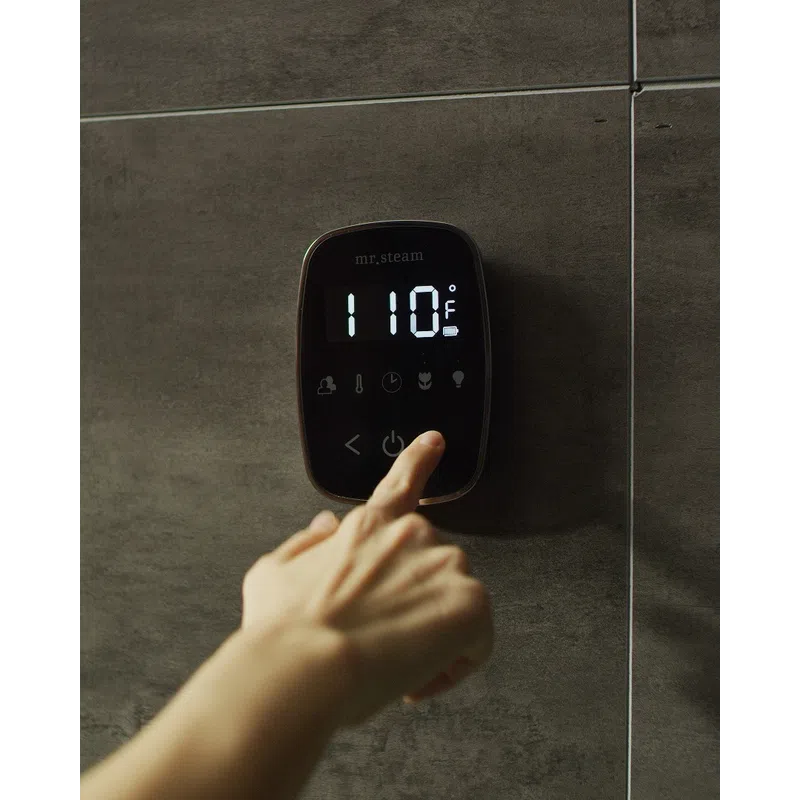 Hand pressing power button on digital steam shower thermostat displaying 110°F on dark tiled wall.