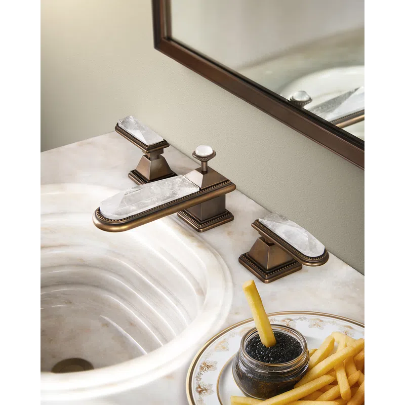 Luxury bathroom sink with gold and marble faucet and a jar of caviar with fries on a decorative plate.