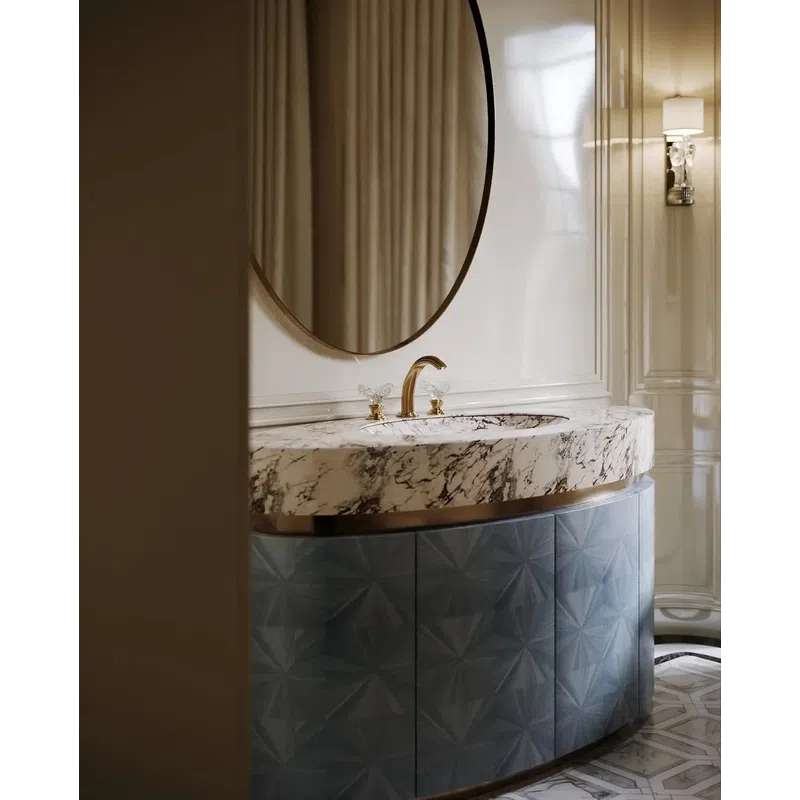 Elegant bathroom vanity with marble countertop, gold faucet, round mirror, and textured blue cabinet.