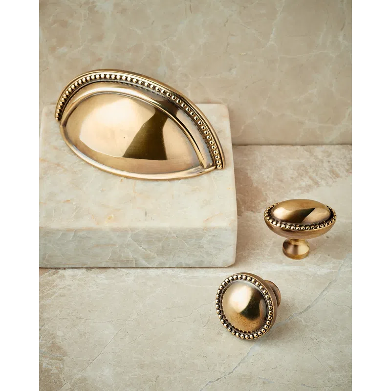 Antique brass cabinet handles and knobs with decorative beaded edges on marble surface.