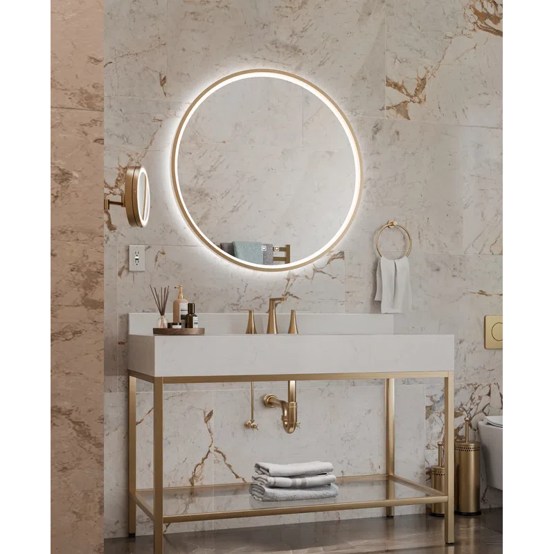 Modern bathroom with a round illuminated mirror, marble walls, gold fixtures, and a minimalist vanity with towels.