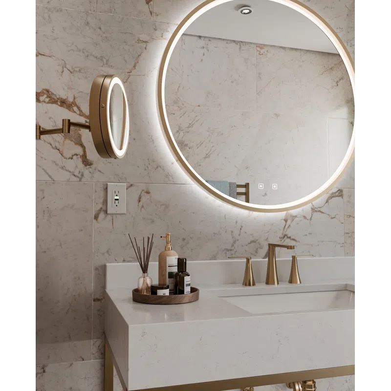 Modern bathroom with a round illuminated mirror, marble walls, white countertop, and gold faucet fixtures.