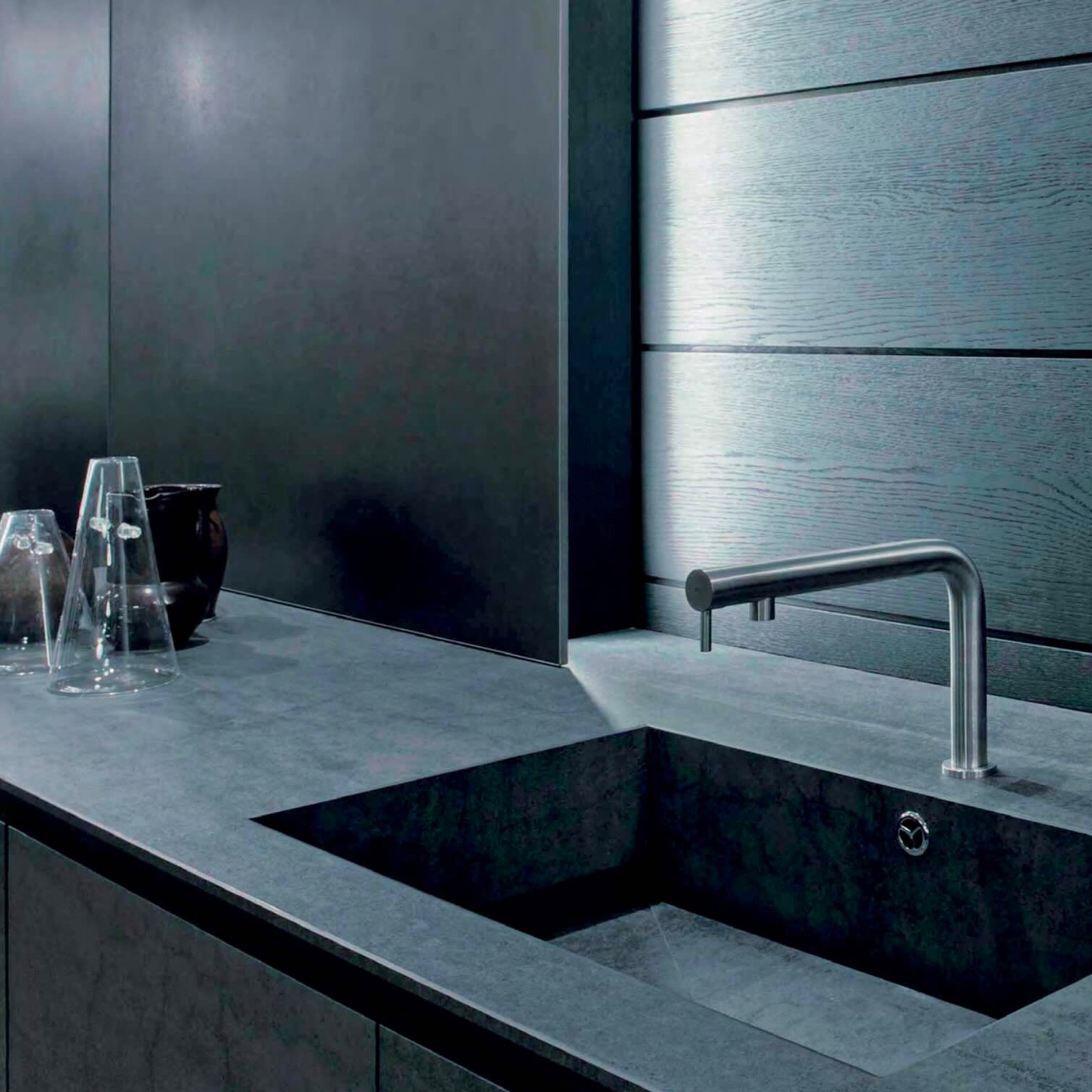 Modern gray kitchen sink with sleek stainless steel faucet and minimalist countertop with glassware and black vase.