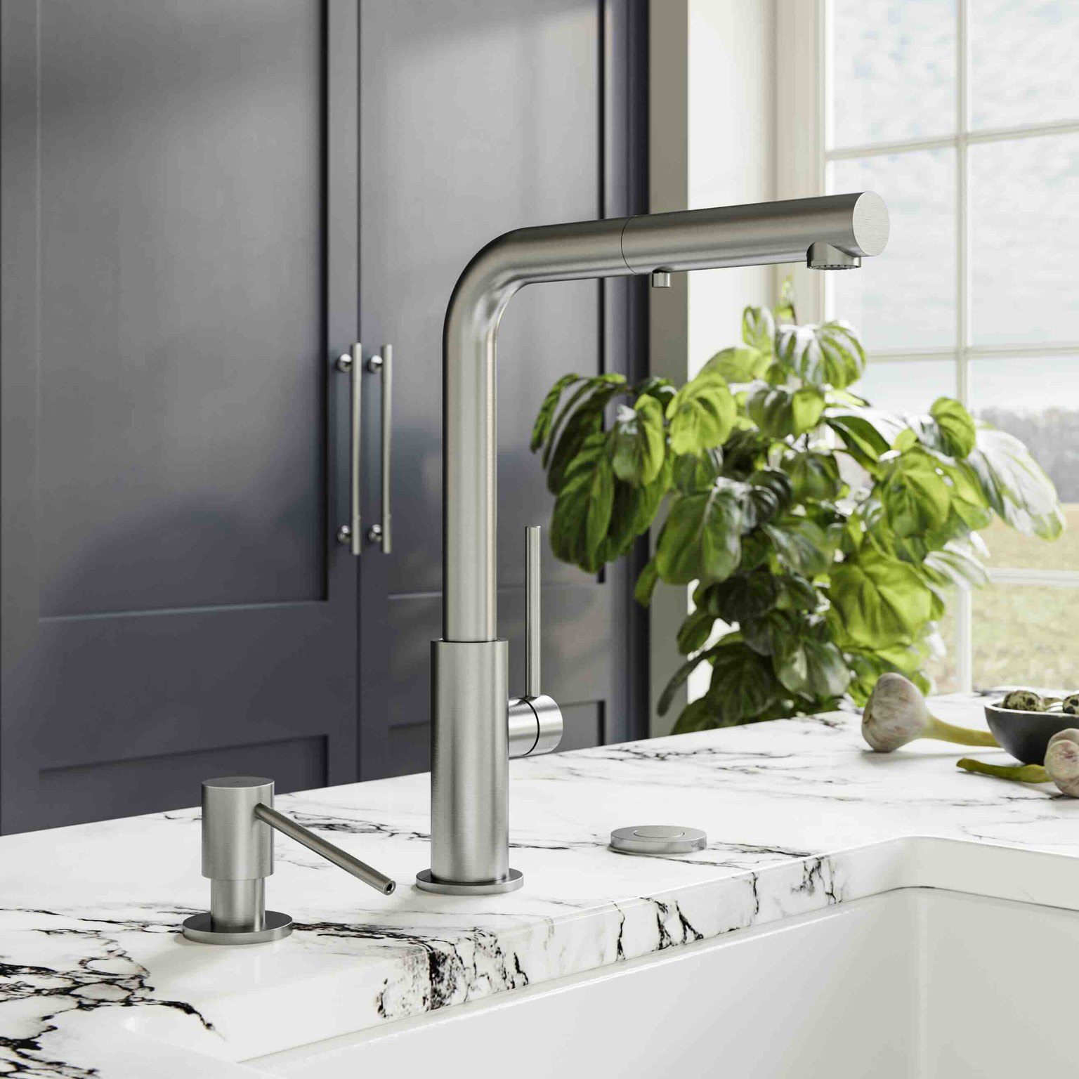 Modern stainless steel kitchen faucet and soap dispenser on white marble countertop with plant in background