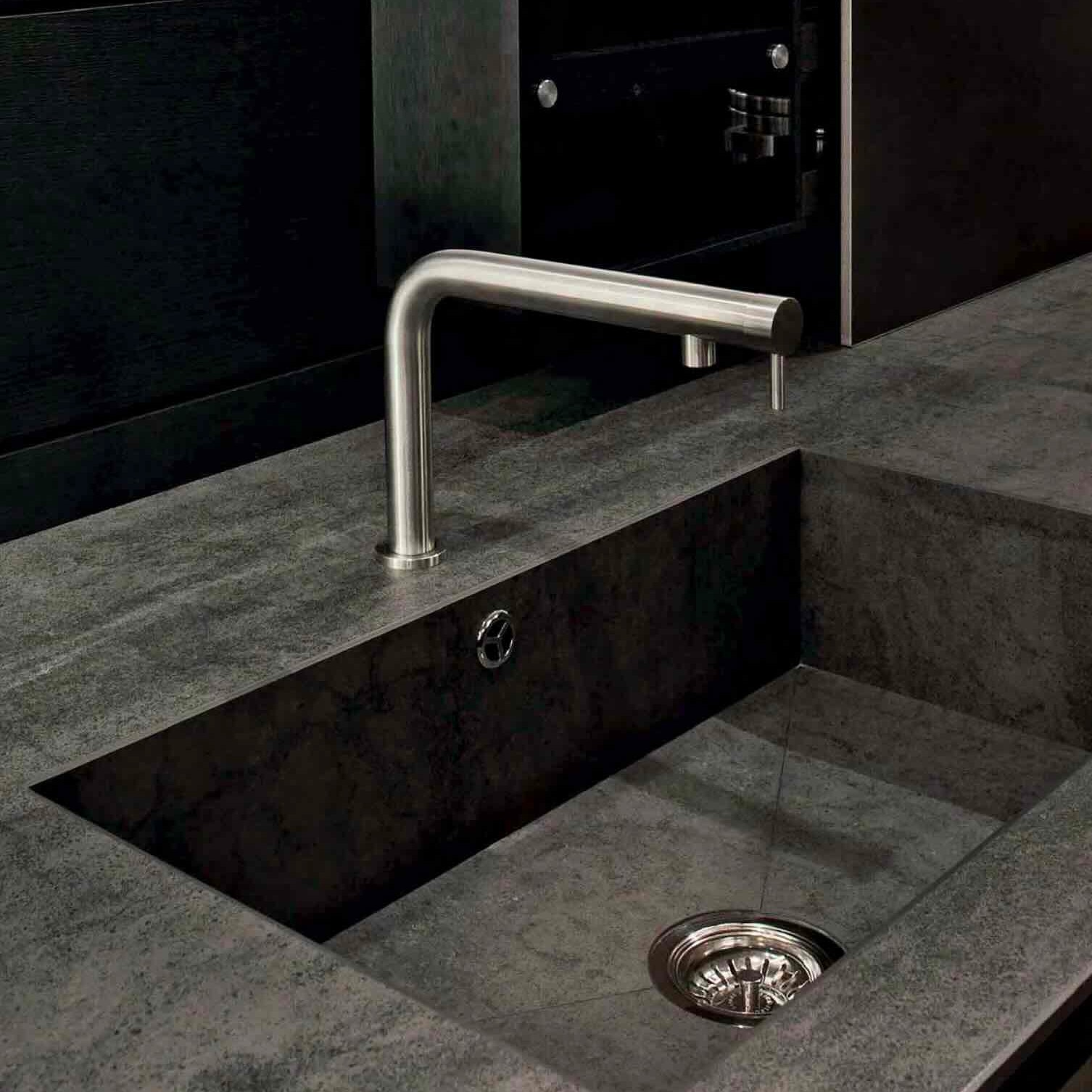 Modern minimalist kitchen sink with dark stone countertop and sleek stainless steel faucet.