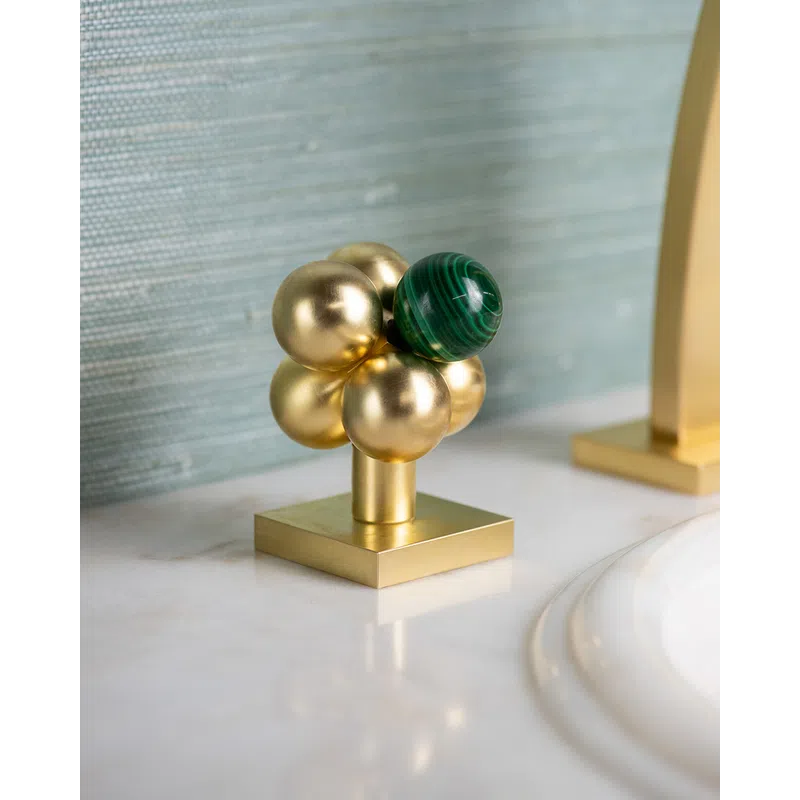 Decorative gold and green spherical cluster sculpture on a marble bathroom countertop near sink.