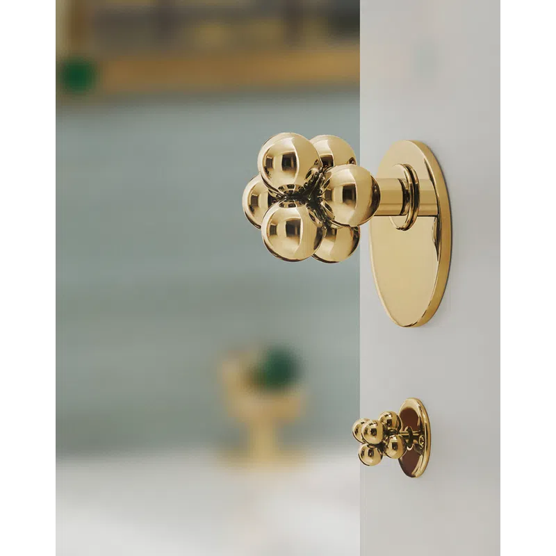 Modern gold metal knobs with spherical design mounted on white door or cabinet.