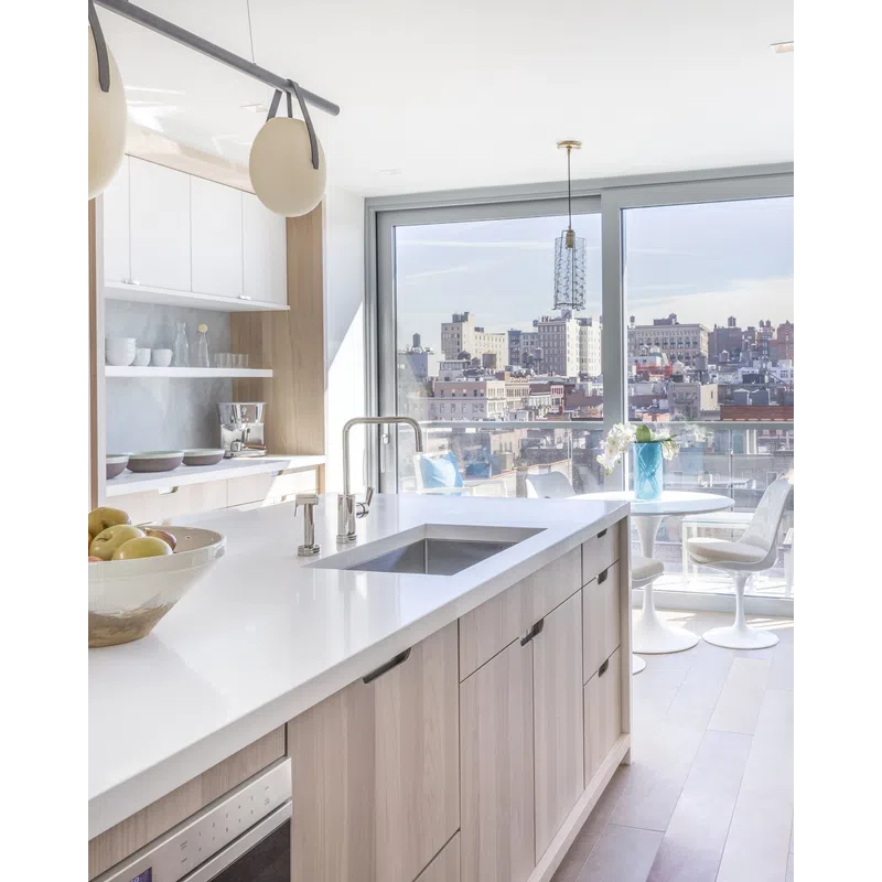Bright modern kitchen with white countertops, wood cabinets, large window, city view, and dining area with chairs.