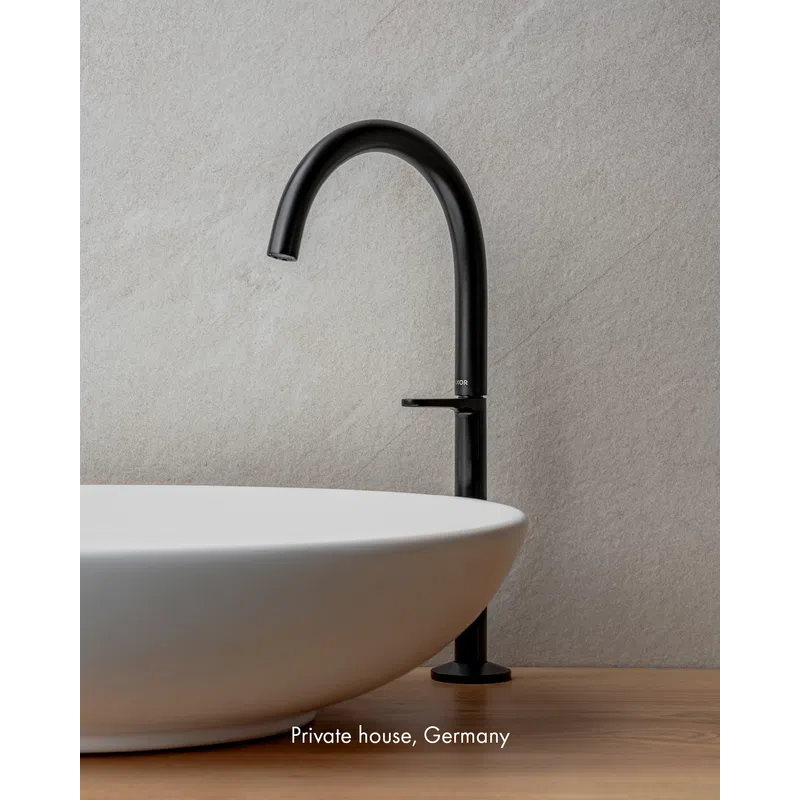 Modern black faucet with a round white ceramic sink on wooden countertop against textured light wall.