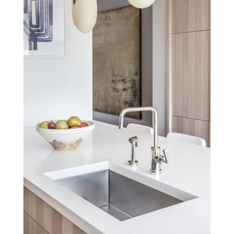 Modern kitchen countertop with stainless steel sink, chrome faucet, and a bowl of fruit on white surface.